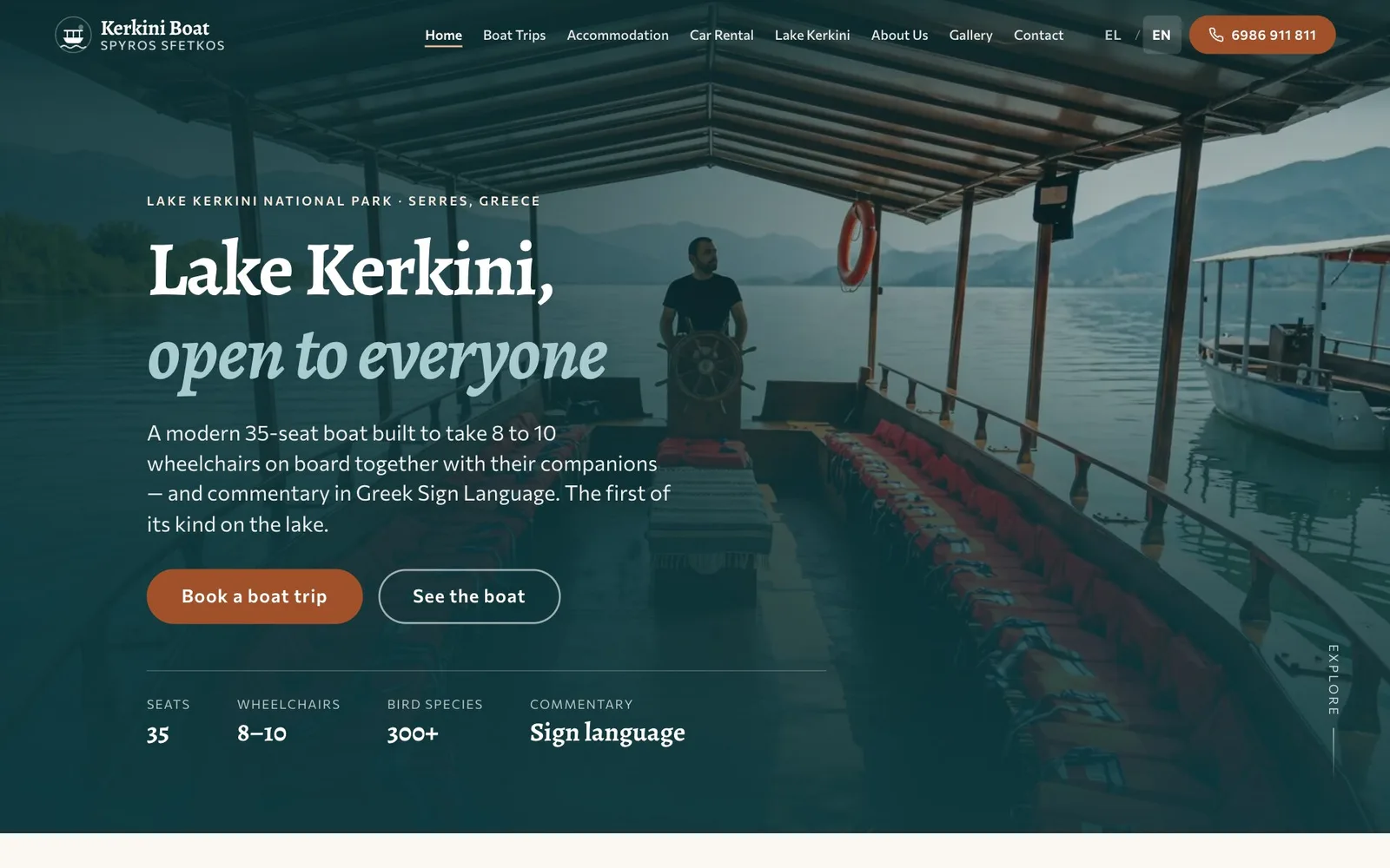 The Kerkini Boat home page: below the line "Lake Kerkini National Park · Serres, Greece", the headline "Lake Kerkini, open to everyone", its second line in pale italic, over a dark-tinted photograph of the boat's covered deck with the skipper at the wheel and the lake and mountains beyond; under it, a short introduction, a rust "Book a boat trip" button, an outlined "See the boat" button and four figures: 35 seats, 8–10 wheelchairs, 300+ bird species and sign-language commentary.