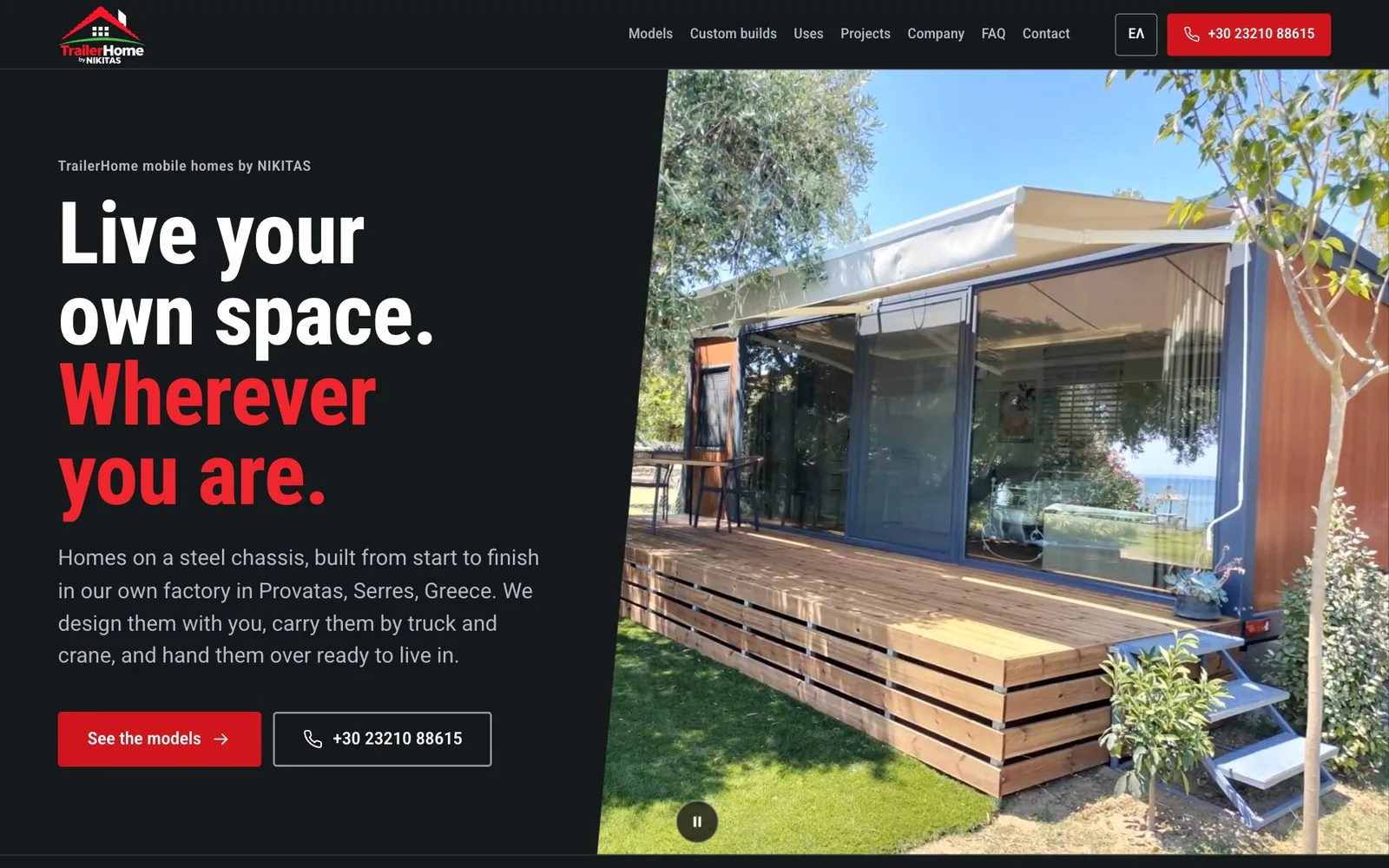 The TrailerHome home page: the headline "Live your own space. Wherever you are.", its second sentence in red, beside a mobile home with glass walls, wood-look cladding and a timber deck under olive trees, with a red "See the models" button and an outlined phone button below the text.
